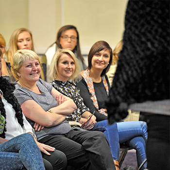 Members of audience at fashion show smiling as they look at model on catwalk